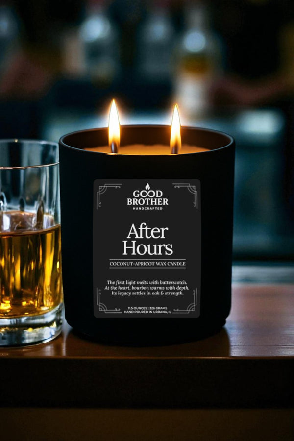 Candle labeled 'After Hours' by 'Good Brother' next to a glass of whiskey on a wooden surface.