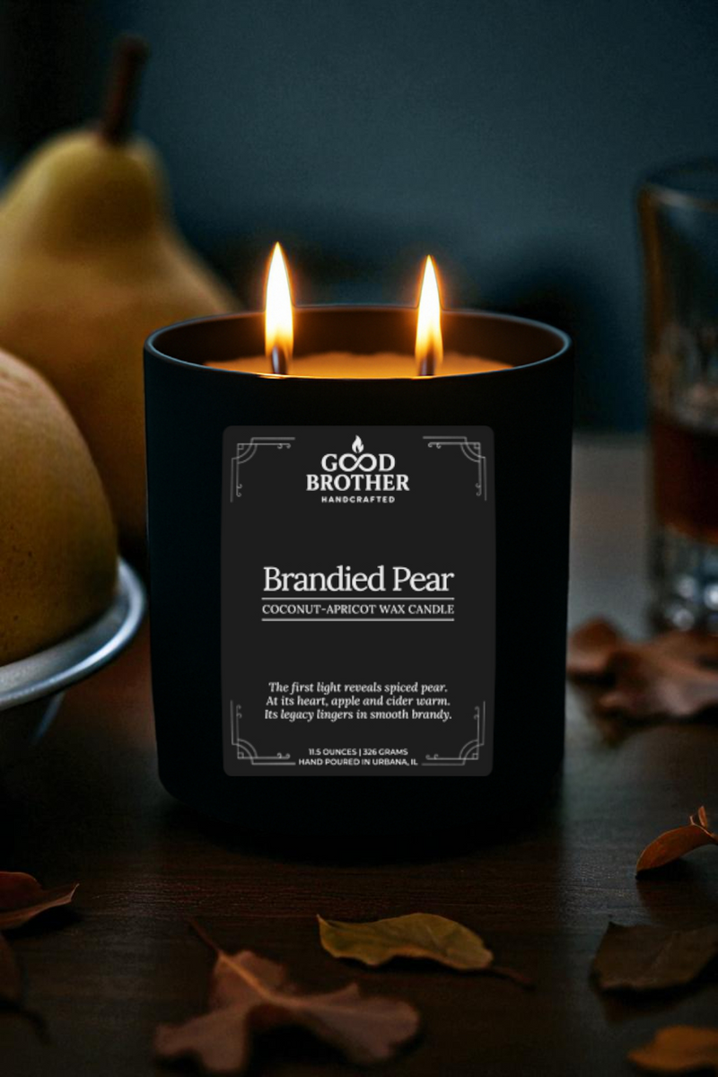 Candle labeled with 'Brandied Pear' by Good Brother on a dark surface with pears and a glass.
