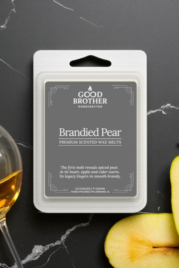 Brandied Pear scented wax melt packaging with a glass of brandy and pear slices on a dark surface.