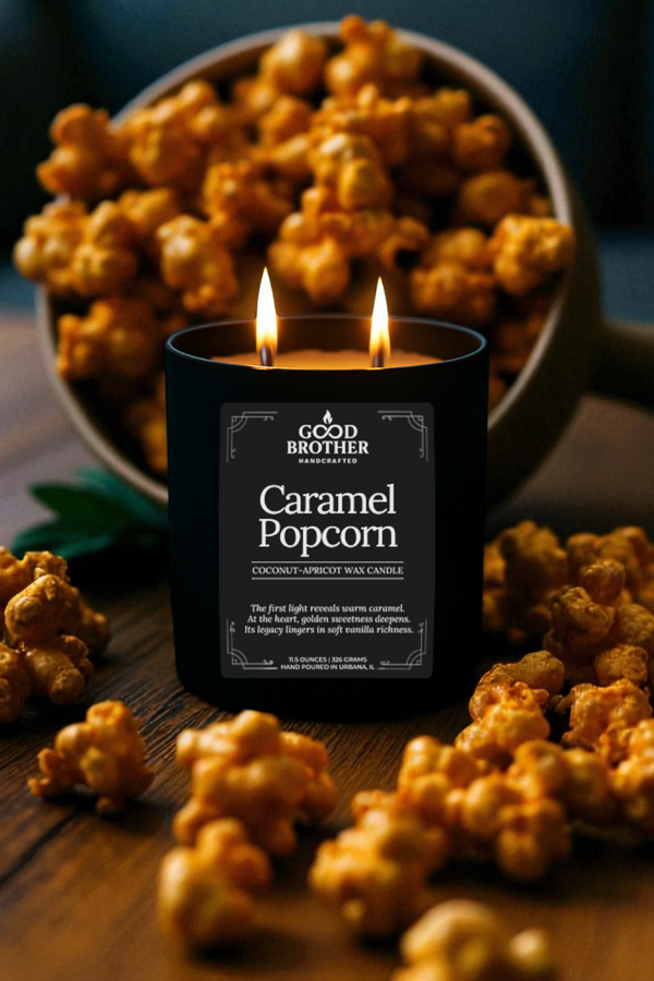 Candle labeled 'Caramel Popcorn' by 'Good Brother' with caramel popcorn around on a wooden surface.