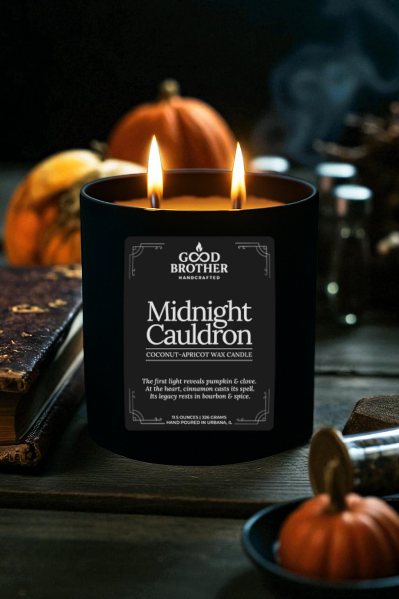 Candle labeled 'Midnight Cauldron' by Good Brother next to a bound spell book with pumpkins and a dark background. 
