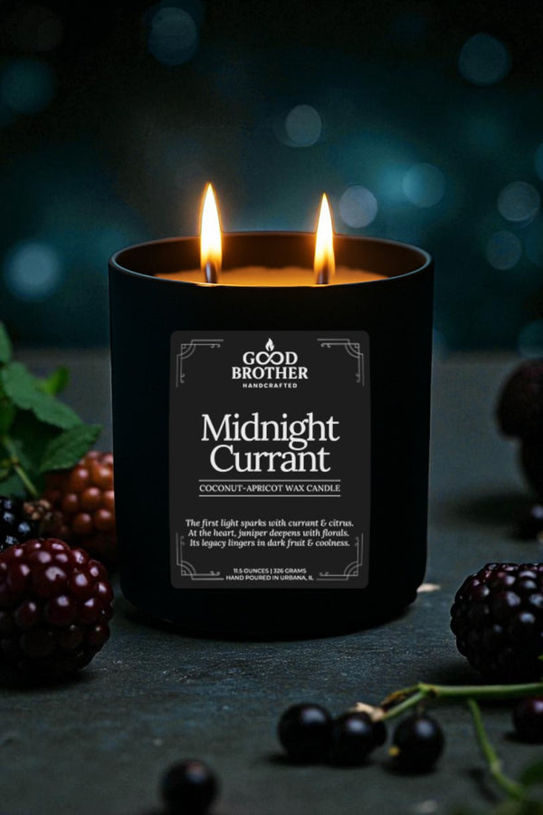 Black candle labeled 'Midnight Currant' by Good Brother surrounded by blackberries on a dark background.