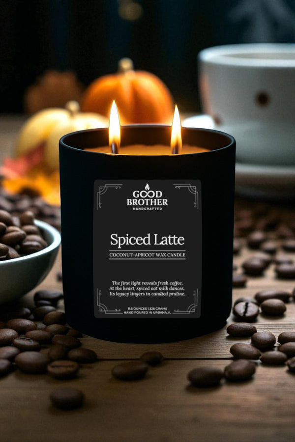 Black candle labeled 'Spiced Latte' by 'Good Brother' with coffee beans and pumpkins in the background.
