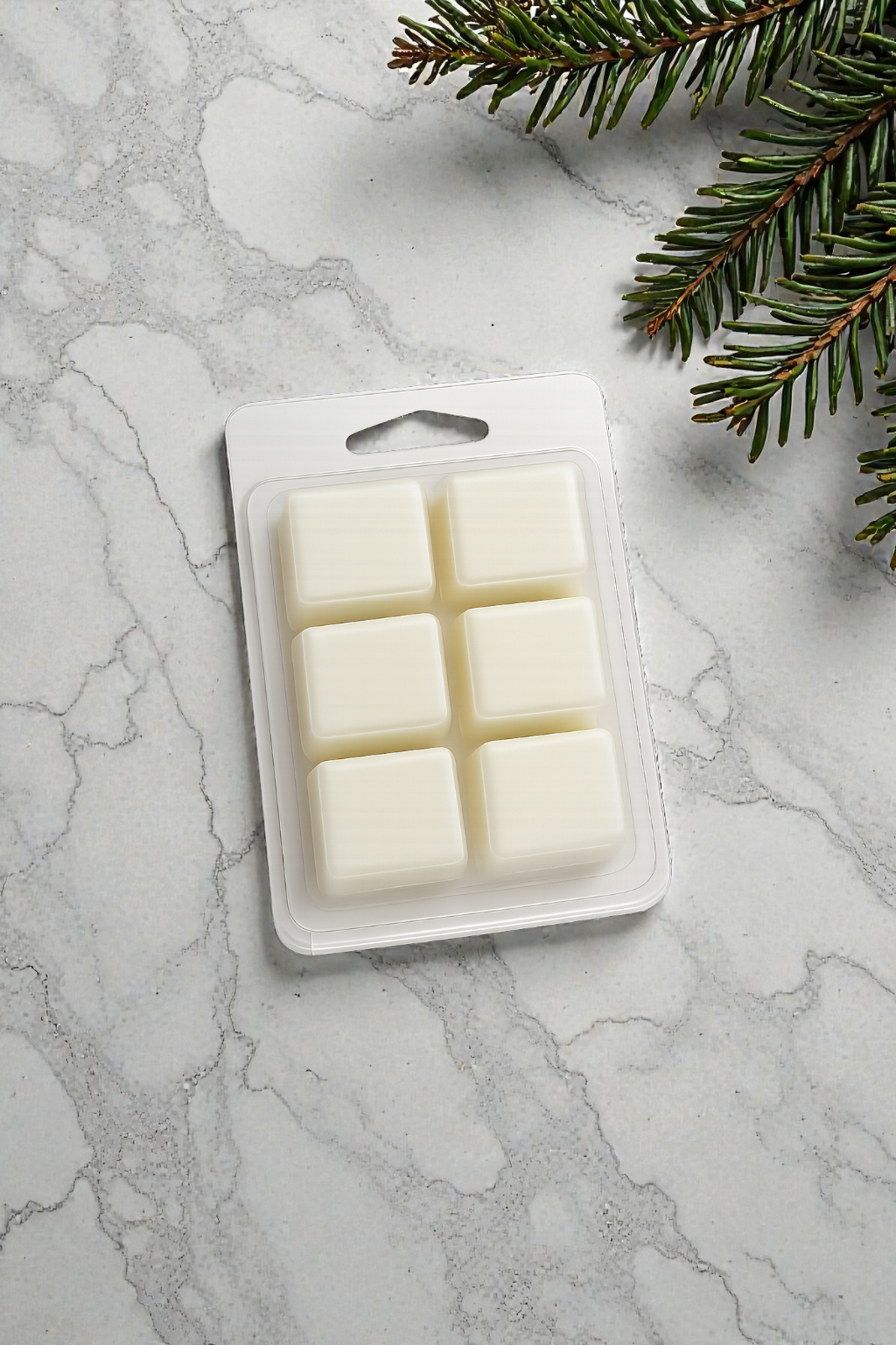 Pack of six white wax melts on a marble surface with a sprig of greenery.