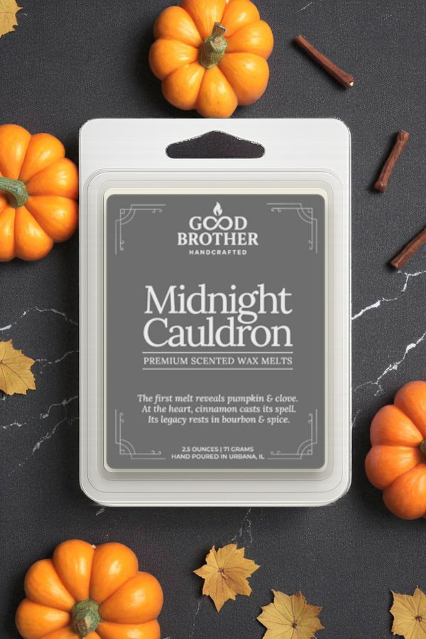 Midnight Cauldron wax melt packaging with pumpkins and cinnamon sticks on a dark surface.